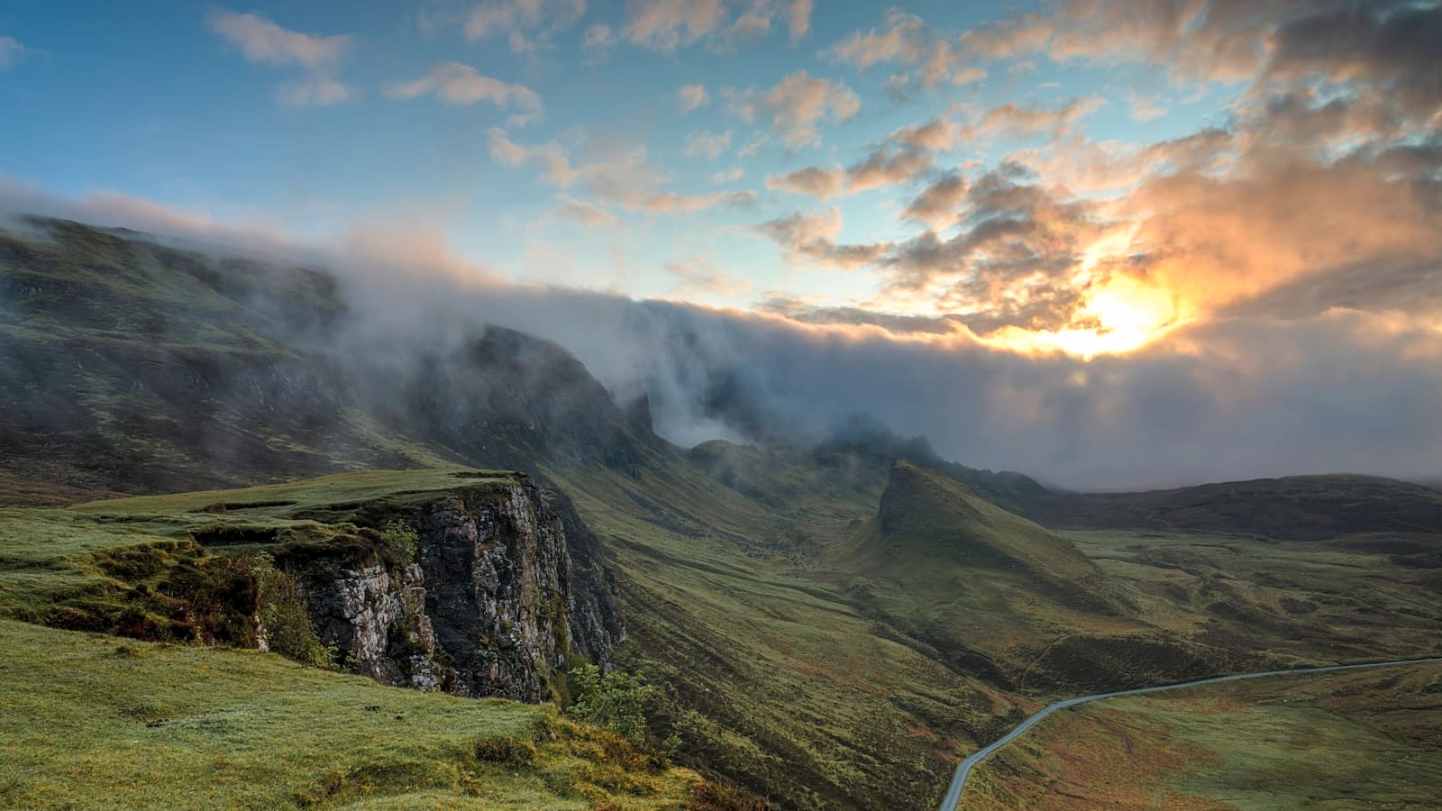 Sunset light and clouds spilling over a steep mountain ridgeline