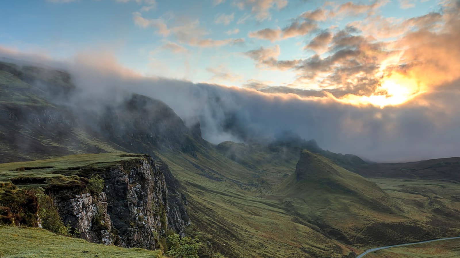 Sunset light and clouds spilling over a steep mountain ridgeline