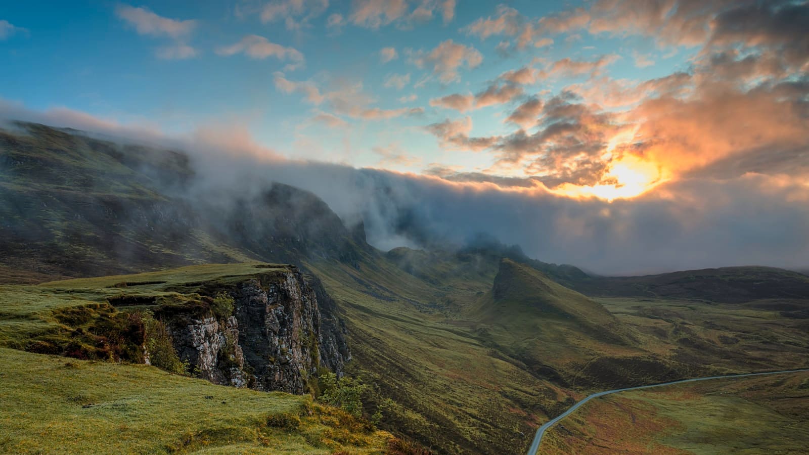 Sunset light and clouds spilling over a steep mountain ridgeline
