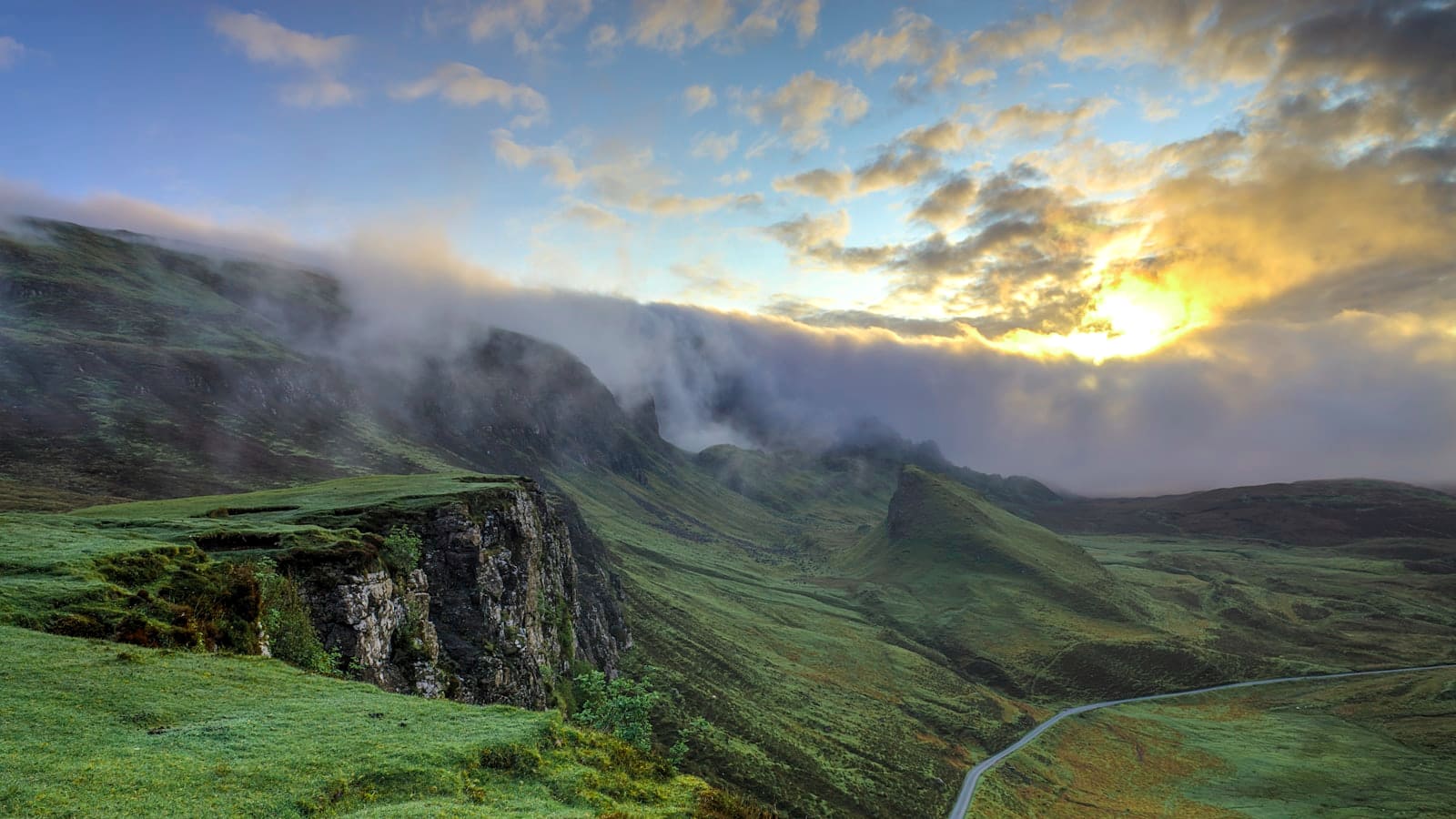 Sunset light and clouds spilling over a steep mountain ridgeline