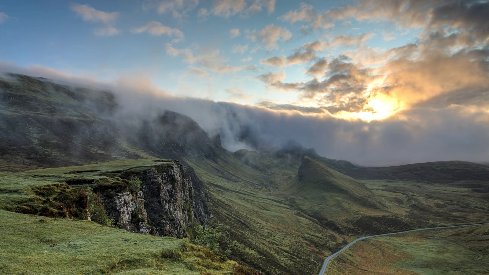 Sunset light and clouds spilling over a steep mountain ridgeline