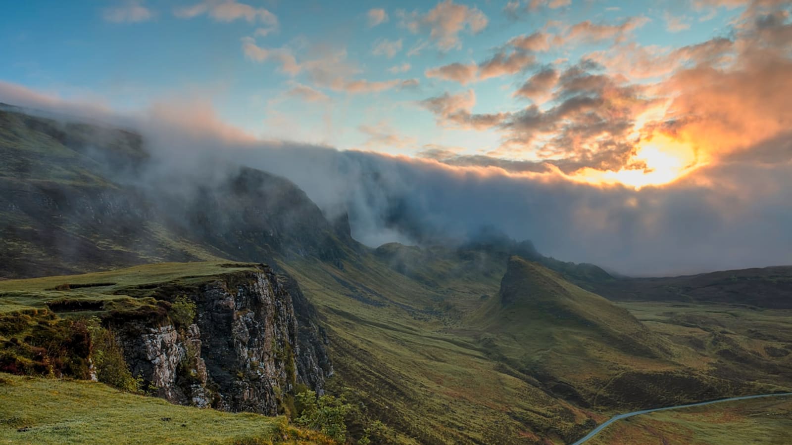 Sunset light and clouds spilling over a steep mountain ridgeline