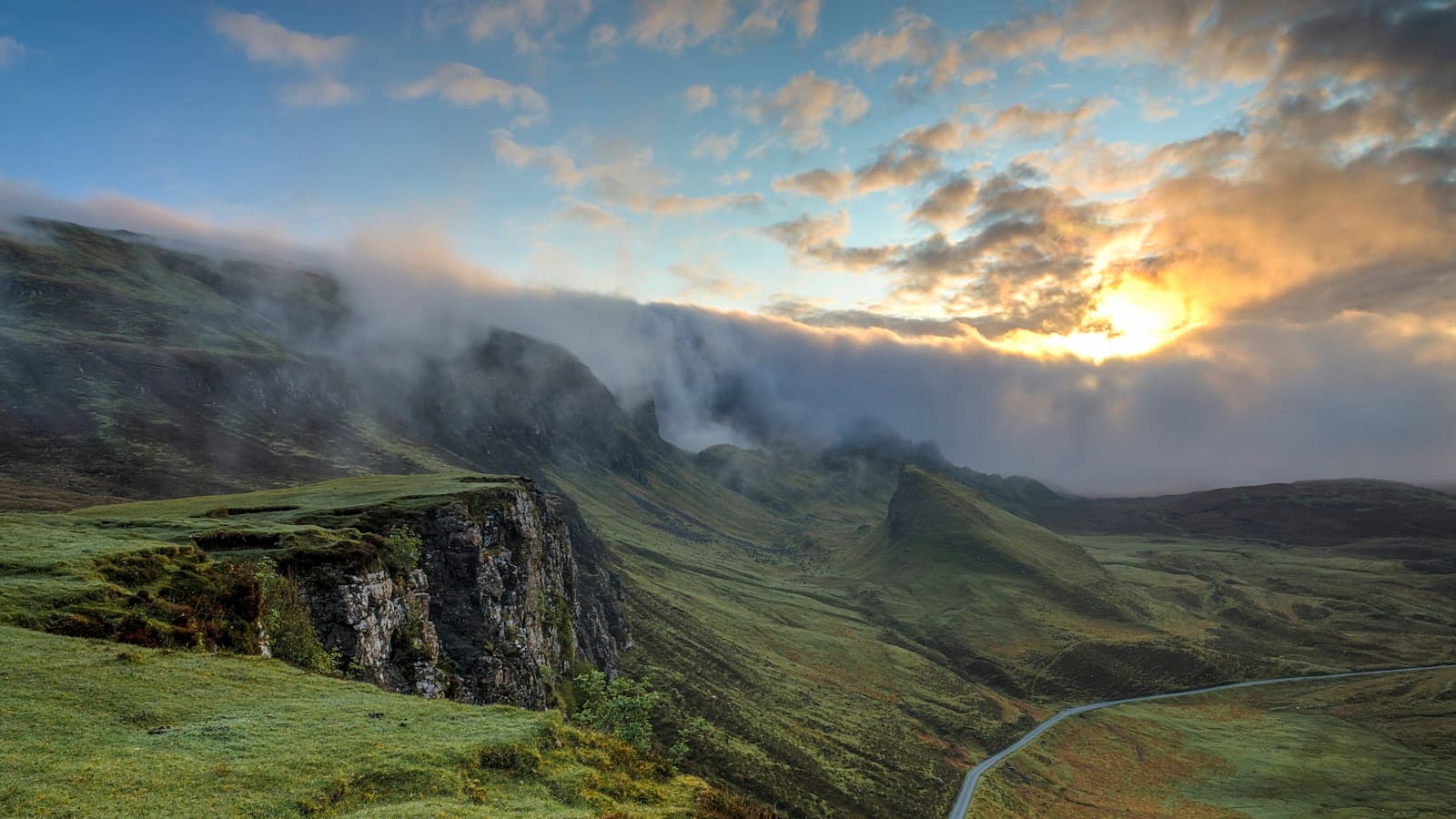 Sunset light and clouds spilling over a steep mountain ridgeline